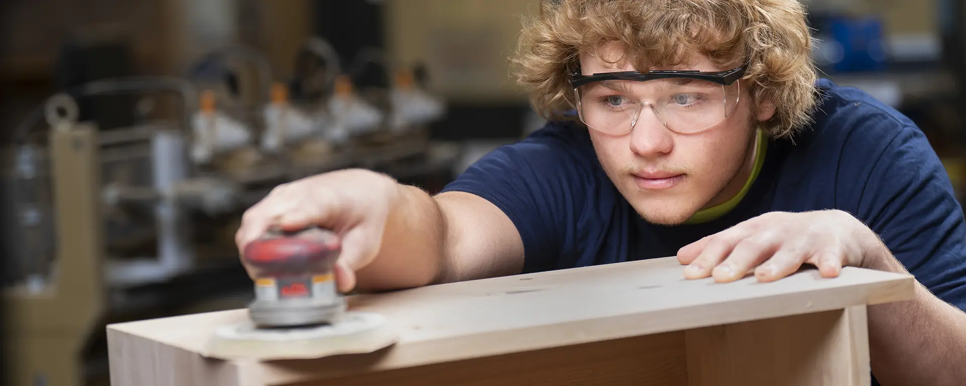 A millwork student sands a cabinet.