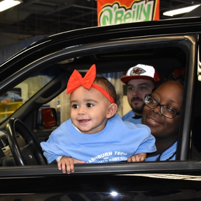 family with baby looking out car window inside Tech automotive garage