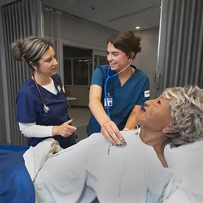 student with instructor next to dummy patient in hospital bed