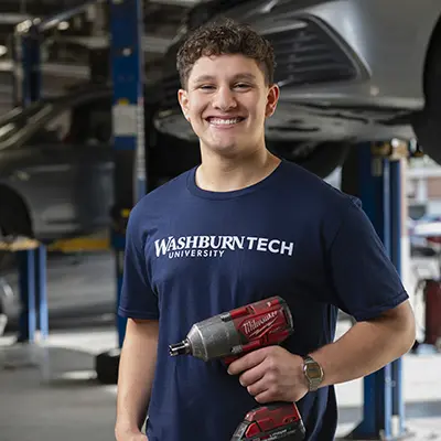 An automotive student holds a drill while posing for a photo.